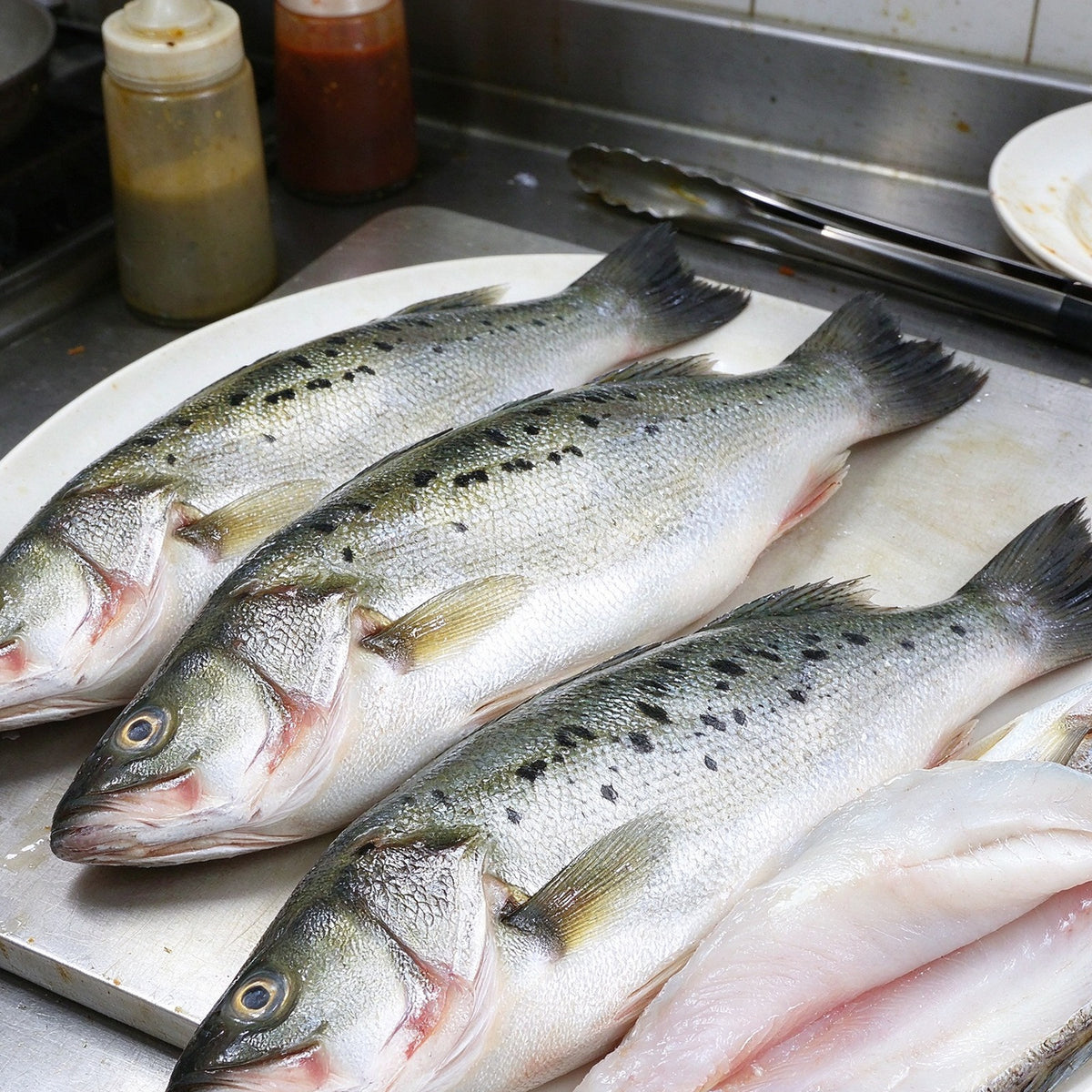 Whole sea bass beside a pale fillet on a white plate