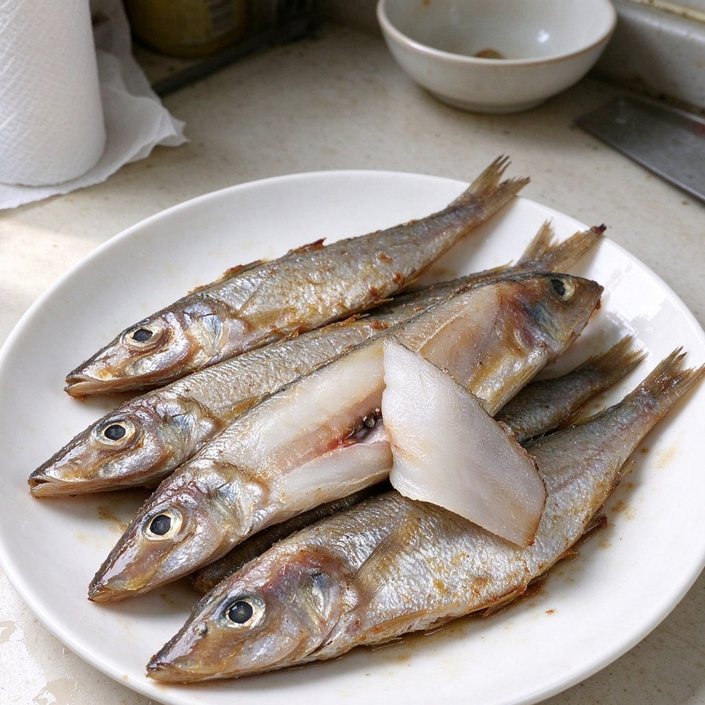 Silver whole sardines laid out on a steel counter