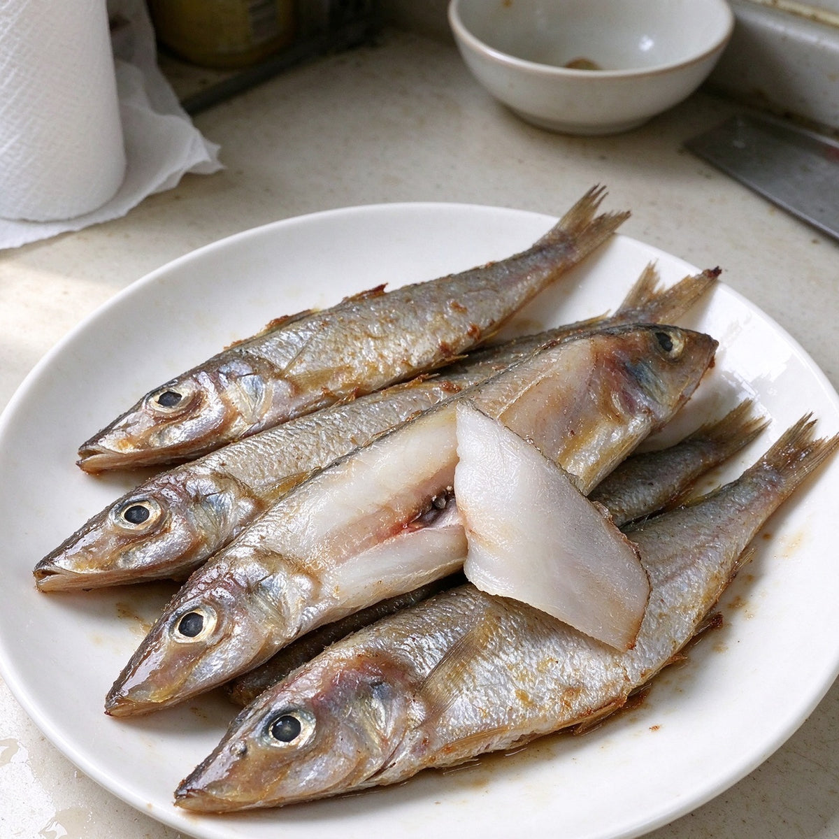 Silver whole sardines laid out on a steel counter