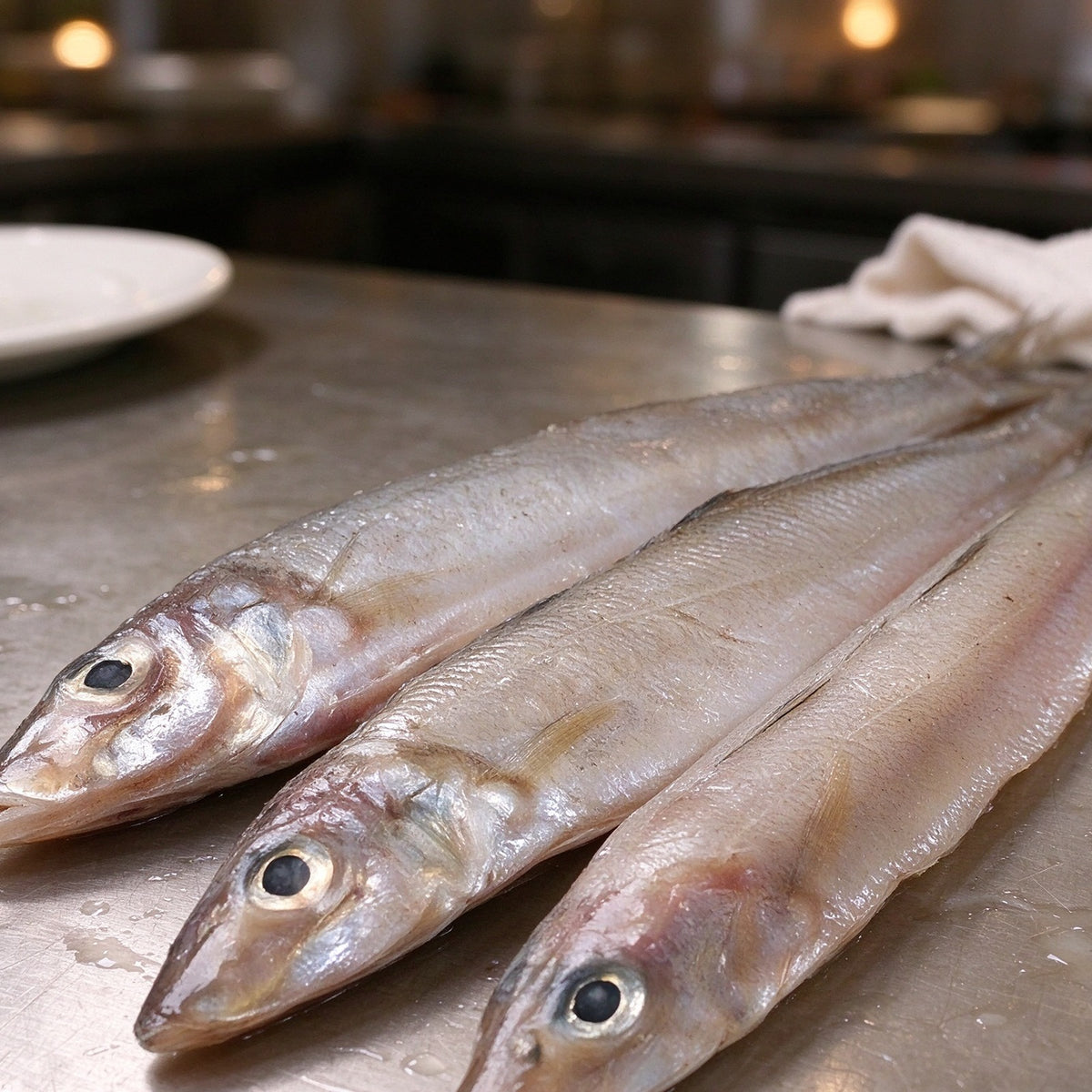 Silver whole sardines laid out on a steel counter