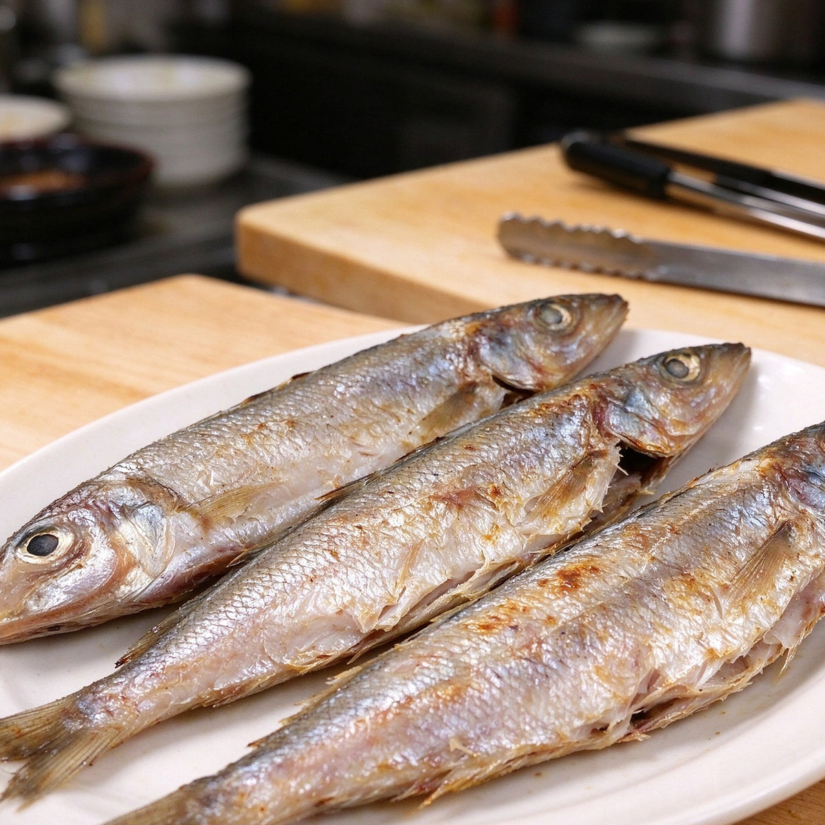 Silver whole sardines laid out on a steel counter